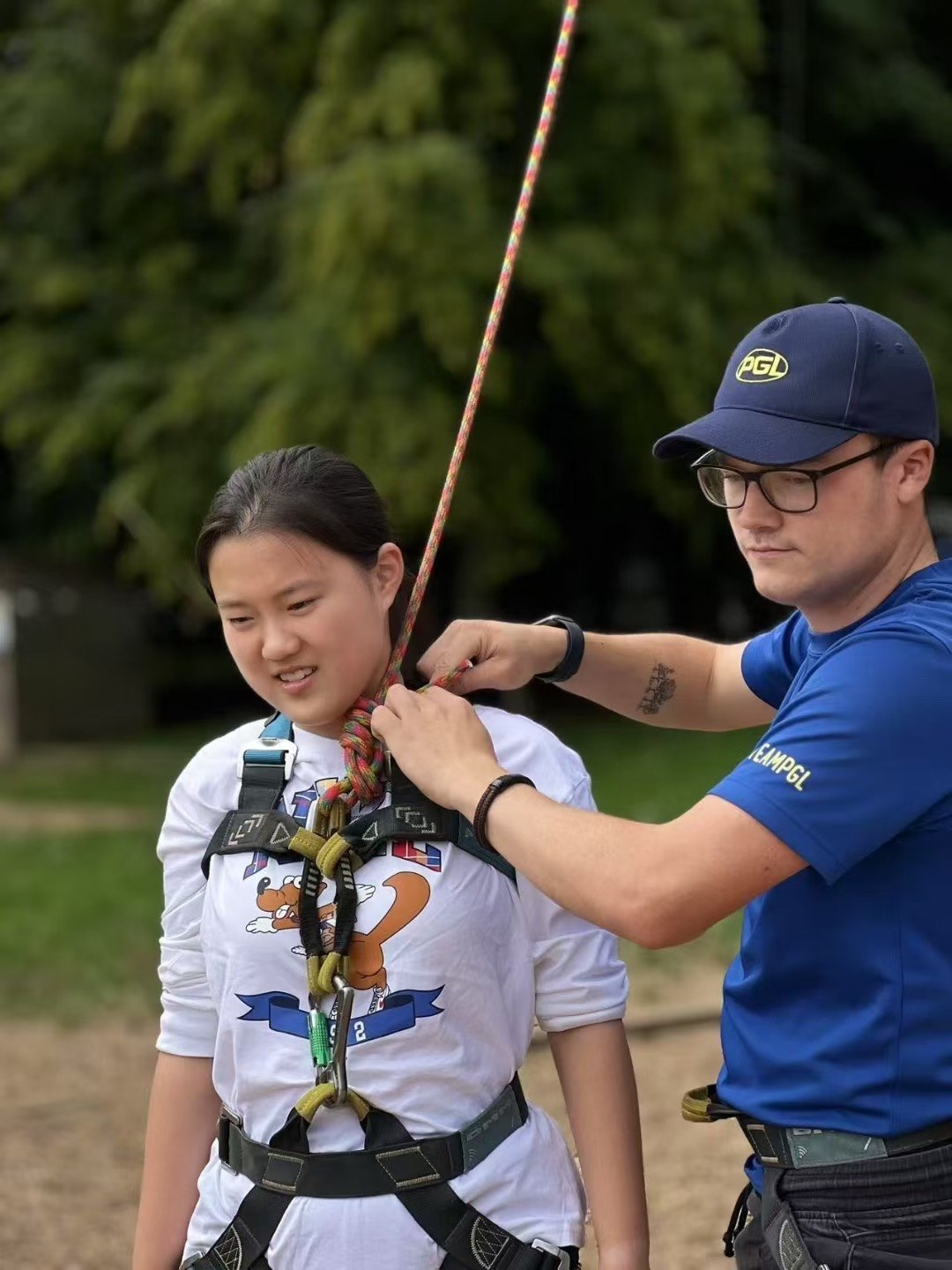 A person helps adjust a participant's rope and harness near the shoulder