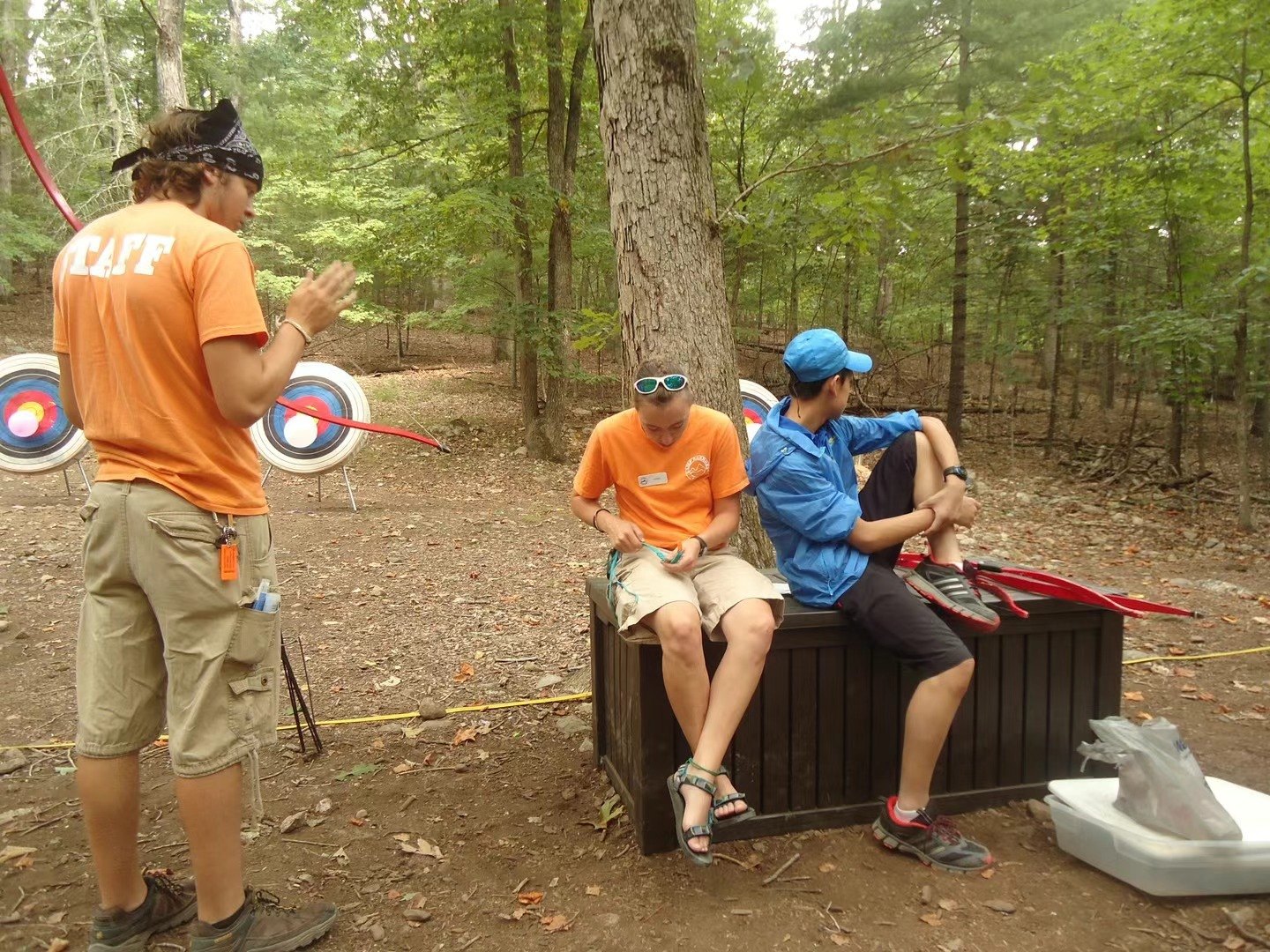 A staff member gestures to seated participants at an activity area among trees