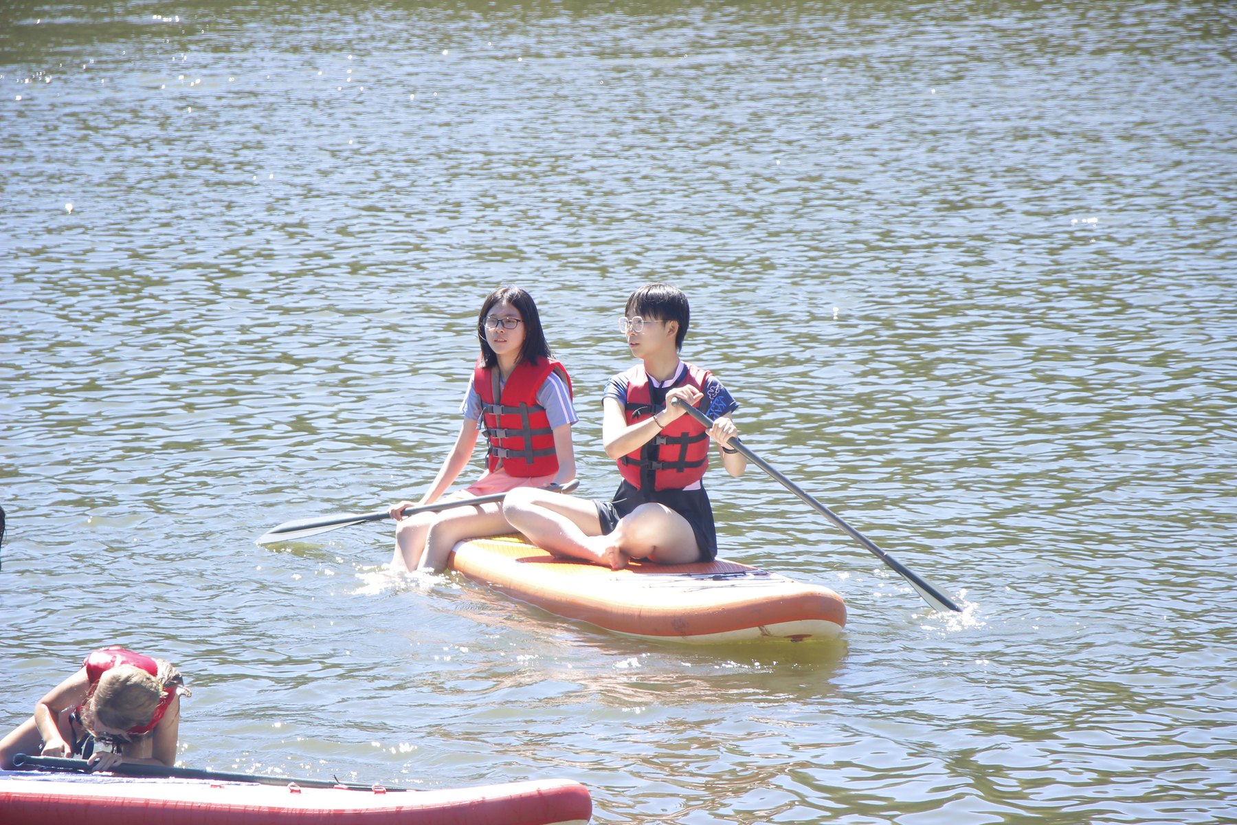 Two participants in life jackets sit on a paddleboard, one holding a paddle